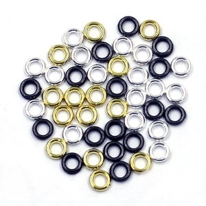 May include: A collection of small, round jump rings in black, silver, and gold. The rings are arranged in a loose pile.