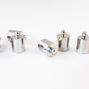 May include: Silver metal end caps with a loop for jewelry making. The end caps are cylindrical and have a smooth finish.
