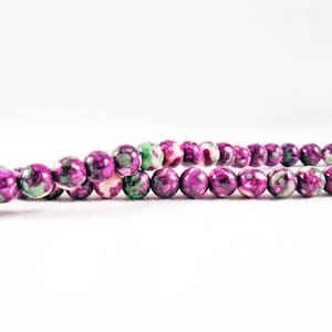May include: A strand of purple, green, and white patterned beads. The beads are round and have a glossy finish.