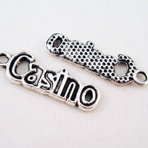 Peut inclure: Deux pendentifs de charme en argent, l'un avec le mot "Casino" et l'autre avec un design texturé.