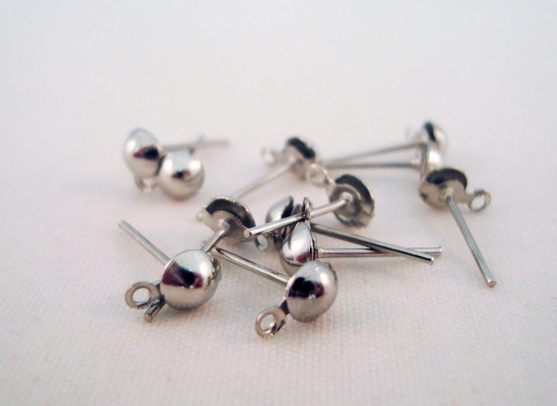 Puede incluir: Primer plano de hallazgos de pendientes de plata con una bola redonda al final de cada poste. Los hallazgos est&aacute;n dispersos sobre una superficie blanca.