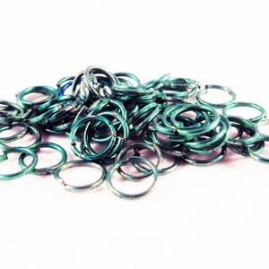 May include: A pile of teal-colored metal jump rings. The rings are all the same size and are arranged in a random pattern.