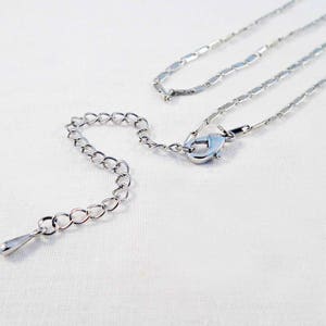 May include: A silver chain necklace with a lobster clasp closure. The chain is made of small, rectangular links.