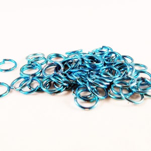 May include: A pile of small, turquoise-colored metal jump rings. The rings are about 1/2 inch in diameter and are perfect for jewelry making.