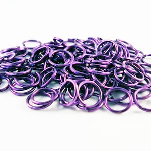 May include: A large pile of purple metal jump rings. The rings are small and round, and they are all the same size.