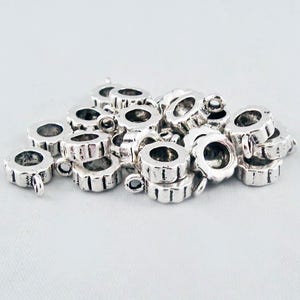 May include: A pile of silver-toned metal bead caps with a decorative edge and a loop on one side.