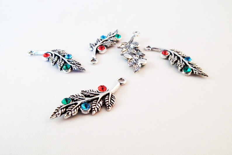 May include: Five silver-toned leaf-shaped charms with red, green, and blue gemstones. Each charm has a loop for attaching to jewelry or other crafts.
