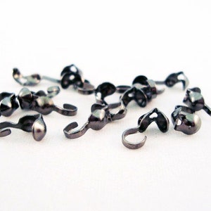 Puede incluir: Un grupo de cierres de metal negro con un gancho en un extremo y un bucle en el otro. Los cierres están dispersos sobre una superficie blanca.