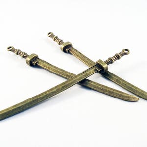 May include: Three antique gold-toned swords with intricate details. The swords are arranged in a criss-cross pattern.