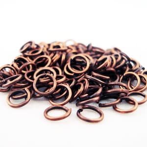May include: A pile of small, copper-coloured jump rings. The rings are all the same size and are arranged in a random pattern.