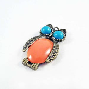 May include: A bronze owl pendant with a coral-coloured stone and turquoise blue accents.