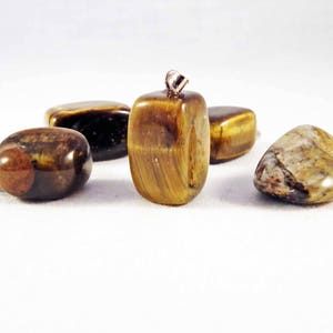 Può includere: Quattro pietre di occhio di tigre, una con una ghiera d'argento, su una superficie bianca. Le pietre sono marroni, dorate e nere con un effetto scintillante.