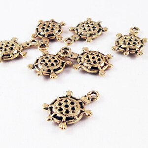 May include: Seven gold-toned turtle charms with a detailed design. The charms have a loop at the top for attaching to jewelry or other crafts.