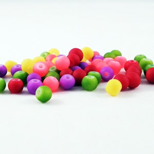 Può includere: Un mucchio di perline rotonde colorate in tonalità di verde, giallo, rosa, rosso e viola. Le perline sono fatte di un materiale liscio e opaco.