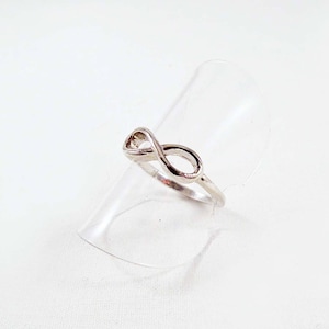 May include: A silver infinity ring on a clear display stand. The ring is a simple design with a smooth finish.