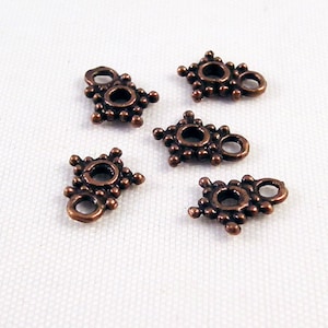 May include: Five copper-colored metal connector charms with a decorative design. Each charm has two holes for attaching to jewelry or other crafts.
