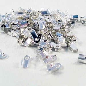 May include: A large pile of silver-toned metal clasps, also known as crimp beads, used for jewelry making.
