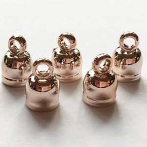 May include: Five rose gold metal cord end caps with a loop at the top.
