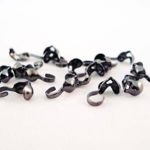 以下が含まれることがあります： 丸みを帯びた端と反対側にフックが付いた黒い金属製の留め具がいくつかあります。留め具は白い表面に散らばっています。