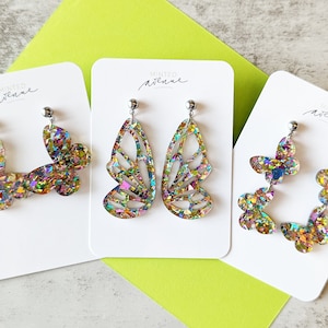 May include: Three pairs of iridescent butterfly earrings on white cards with the text "Minted Avenue" printed on each card.