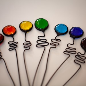 Peut inclure: Un ensemble de huit tiges de fil de fer surmontées de verre coloré. Les sommets en verre sont rouge, orange, jaune, vert, bleu, indigo et violet. Les tiges de fil de fer sont noires et ont un design bouclé.