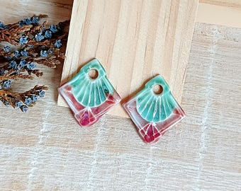 Puede incluir: Un par de pendientes cuadrados con un diseño geométrico. Los pendientes presentan un patrón en forma de abanico turquesa en la parte superior, que se fusiona con una base roja y transparente. Cada pendiente tiene un pequeño agujero en la parte superior.
