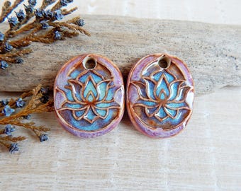 May include: Two ceramic pendants with a blue lotus flower design. The pendants are round and have a brown glaze with a purple hue.