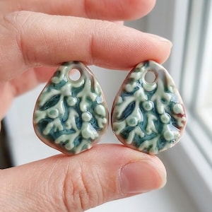 May include: Two teardrop-shaped ceramic pendants featuring a raised, branching coral-like pattern in pale green against a deep teal background. Each pendant has a smooth, glossy finish and a single circular hole at the top for hanging.