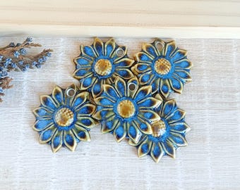 May include: Five ceramic flower pendants with a blue and brown glaze. Each pendant has a hole for hanging. The flowers are arranged on a light wood-grain surface.