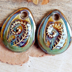 Puede incluir: Dos colgantes de cer&aacute;mica en forma de l&aacute;grima con un dise&ntilde;o de helecho. Los colgantes tienen un agujero en la parte superior para ensartar. La combinaci&oacute;n de colores incluye tonos de verde, marr&oacute;n y azul, con un acabado brillante. El dise&ntilde;o del helecho es en relieve.
