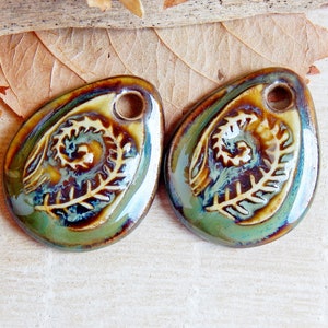 Puede incluir: Dos colgantes de cer&aacute;mica con forma de l&aacute;grima. Cada colgante presenta un dise&ntilde;o de helecho en relieve en crema sobre un fondo esmaltado verde, marr&oacute;n y azul. Un peque&ntilde;o agujero en la parte superior para ensartar. Suministros para la fabricaci&oacute;n de joyas.