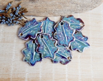 May include: A collection of eight ceramic leaf charms in shades of blue, purple, and white. The leaves have a textured, hand-painted look and are perfect for adding a touch of nature to jewellery or crafts.