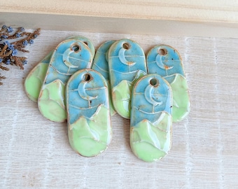 May include: Six ceramic pendants with a blue and green glaze. Each pendant features a crescent moon and mountain design.