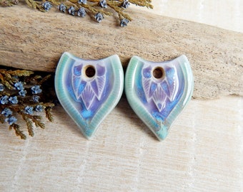 May include: Two ceramic pendants with a teal, purple, and white glaze. The pendants are shaped like a teardrop with a hole at the top for stringing.