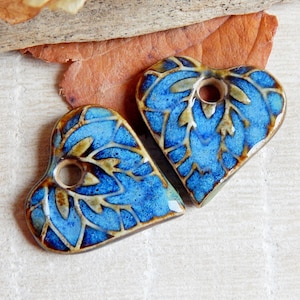 May include: Two blue and brown ceramic heart-shaped pendants with a decorative pattern and a hole for hanging.