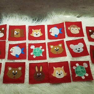 Könnte beinhalten: Ein Set mit 16 Filzquadraten mit gestickten Tier- und Fischmotiven. Jedes Quadrat ist rot mit einem anderen Tier oder Fisch in der Mitte. Zu den Tieren gehören ein Bär, ein Hund, eine Katze, ein Kaninchen, eine Schildkröte, eine Maus und ein Affe.