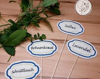 May include: Four white oval-shaped plant markers with blue and green embroidery. The markers are labeled "Salbei", "Lavendel", "Schnittlauch", and "Bohnenkraut".