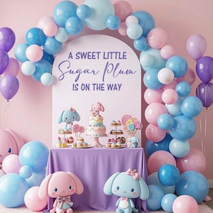 May include: A party display featuring a balloon arch in shades of blue, pink, and purple surrounding a sign that reads A SWEET LITTLE Sugar Plum IS ON THE WAY. A table with a purple cloth holds a tiered cake, cupcakes, and plush bunny figures.