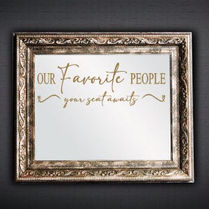 May include: A gold-colored ornate frame with a white background and the text "OUR Favorite PEOPLE your seat awaits" in gold lettering.