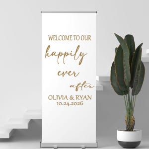 May include: A white retractable banner with gold text that reads "WELCOME TO OUR happily ever after OLIVIA & RYAN 10.24.2026". A potted plant with large green leaves sits to the right.
