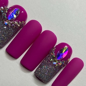 May include: A set of long, pink, matte press-on nails with silver glitter and rhinestones on the accent nails.