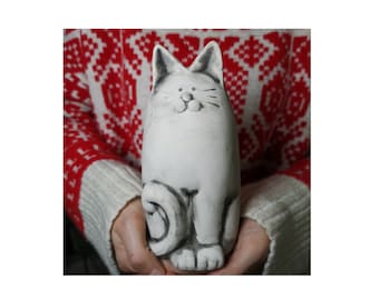 May include: A white ceramic cat figurine with black painted details. The cat is sitting with its tail curled around its legs and has a friendly expression on its face.
