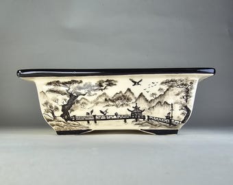 May include: A rectangular ceramic planter with a black rim and a white background. The planter features a black and white ink drawing of a Japanese landscape with mountains, trees, a bridge, and a pagoda.