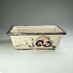 May include: A rectangular ceramic bonsai pot with a black and white dragon design and a red and white moon. The pot has a black rim and a white background.