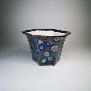 Puede incluir: Una maceta hexagonal de cerámica con interior blanco y exterior azul oscuro con círculos iridiscentes azules y amarillos.