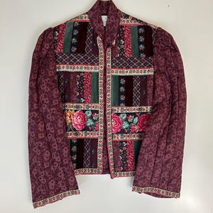 Könnte beinhalten: Gesteppte Jacke mit Patchwork-Design. Die Jacke hat eine Mischung aus floralen, geometrischen und unifarbenen Mustern in Burgunder-, Grün- und Rosatönen. Die Ärmel sind einfarbig burgunderfarben mit floralem Druck.