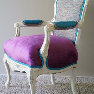 May include: A white, ornately carved chair with a purple velvet seat and teal trim. The chair back is upholstered in a multi-colored fabric.
