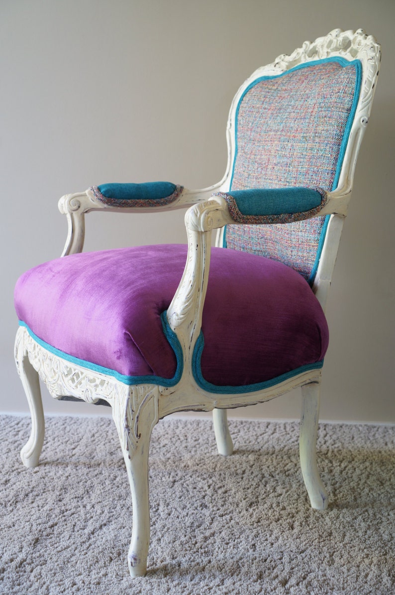 May include: A white, ornately carved chair with a purple velvet seat and teal trim. The chair back is upholstered in a multi-colored fabric.