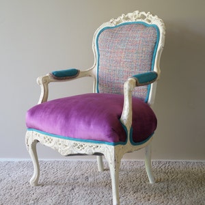 May include: A white, ornately carved armchair with a purple velvet seat and teal trim. The back of the chair is upholstered in a multi-colored patterned fabric.