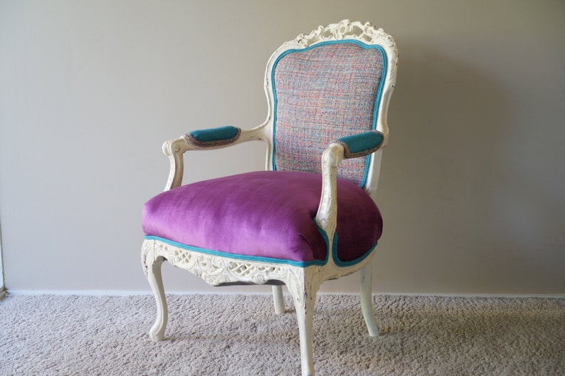 May include: A white, ornately carved armchair with a purple velvet seat and teal trim. The back of the chair is upholstered in a multi-colored patterned fabric.